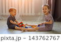 Joyful Siblings Assemble Colorful Toy Bricks Across Living Room Floor, Giggling Cheerfully During Leisure Time While Scattered Small Construction Pieces Represent Possible Home Safety Hazard. 143762767