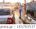 Guy rinsing soapy rear window of silver sedan with pressure washer 143763537