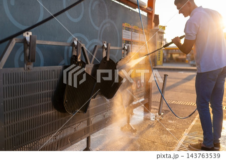 Man washing black floor mats hanging on rack at station Man washing black floor mats hanging on rack at station 143763539