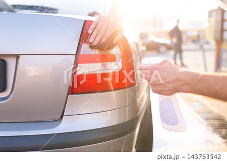 Man spraying detergent and wiping red rear taillight of car 143763542