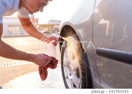 Young man spraying chemical detergent on car tire and wiping rim 143763543