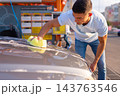 Young man in polo cleaning car hood with yellow sponge 143763546