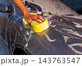 Young man in polo cleaning car hood with yellow sponge 143763547