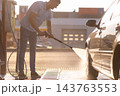 Young man rinsing soapy foam off silver car with high pressure water jet 143763553