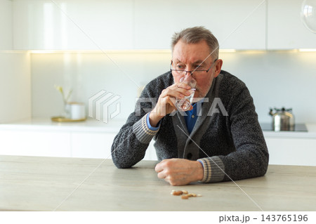Middle aged senior man holding medical pill and glass of water. Mature old senior grandfather taking medication cure pills vitamin. Age prescription medicine healthcare therapy concept Middle aged senior man holding medical pill and glass of water. Mature old senior grandfather taking medication cure pills vitamin. Age prescription medicine healthcare therapy concept 143765196