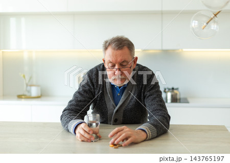 Middle aged senior man holding medical pill and glass of water. Mature old senior grandfather taking medication cure pills vitamin. Age prescription medicine healthcare therapy concept Middle aged senior man holding medical pill and glass of water. Mature old senior grandfather taking medication cure pills vitamin. Age prescription medicine healthcare therapy concept 143765197