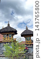 Ornate Balinese temple shrines display tiered thatched roofs beneath dramatic cloudy sky. Carved stonework, painted panels and decorative roof finials define this traditional sacred architecture. 143765800