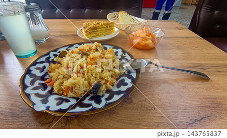 Traditional Uzbek plov pilaf with meat on patterned ceramic plate served on wooden table 143765837