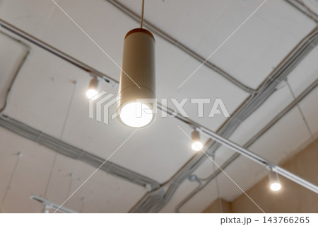 A glowing pendant light hangs from a white ceiling with track lighting A glowing pendant light hangs from a white ceiling with track lighting 143766265