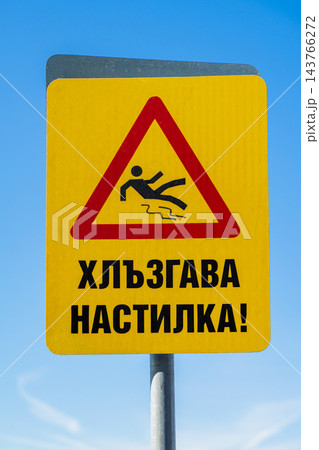 Slippery flooring Warning Sign with Cyrillic Text Against Blue Sky. Slippery surface warning sign with falling person pictogram. Sign in Bulgarian language, in Cyrillic. Translation: Slippery flooring 143766272