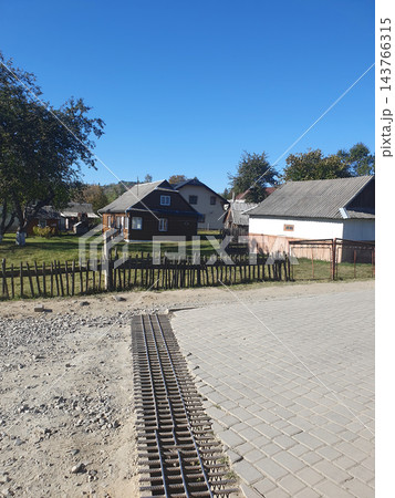 Rural mountain village street with traditional wooden houses, a rustic picket fence and paving stones under a clear blue sky. Carpathian countryside on a sunny autumn day, travel 143766315