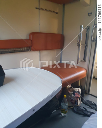 Interior of a train sleeper compartment with orange leatherette seats, a folding table, a luggage rack and a handrail. Rail travel, overnight journey Interior of a train sleeper compartment with orange leatherette seats, a folding table, a luggage rack and a handrail. Rail travel, overnight journey 143766318