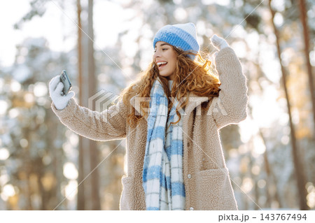 Young woman in a bright hat and scarf with a phone in a snowy forest. Travel, vacation concept. Young woman in a bright hat and scarf with a phone in a snowy forest. Travel, vacation concept. 143767494