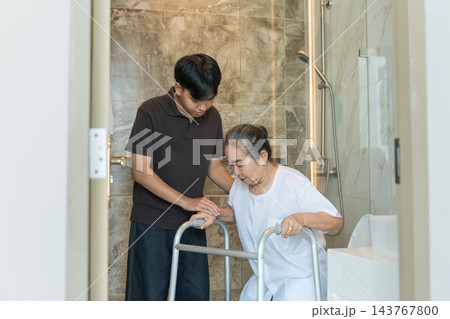 Senior woman assisted by male caregiver in nursing home bathroom for safety. 143767800