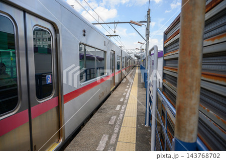 青空の下で狭い駅ホームに停車する赤いラインの銀色の電車と黄色い点字ブロックが続く昼間の日本の鉄道風景 143768702