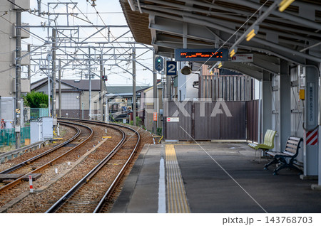 日本の住宅街の駅ホームから見た左へ大きくカーブする複線の鉄道線路と架線設備、青信号とベンチのある風景 143768703