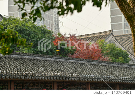 Close-up of the traditional, Chinese classic roof of Chinese building with trees. Chinese historical building with Chinese garden. Travel and nature scene. Building exterior. Close-up of the traditional, Chinese classic roof of Chinese building with trees. Chinese historical building with Chinese garden. Travel and nature scene. Building exterior. 143769401