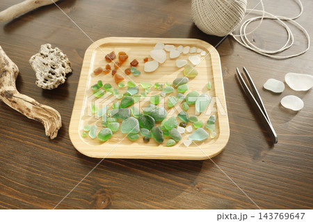 Colorful sea glass collection with driftwood and twine cord on table. Flatlay beachcombing treasures craft materials and tweezers. Sustainable eco zero waste DIY coastal home decor project. 143769647