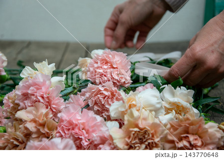 A person is placing pink and white flowers with green stems on a wooden surface. The setting is indoors and bright 143770648
