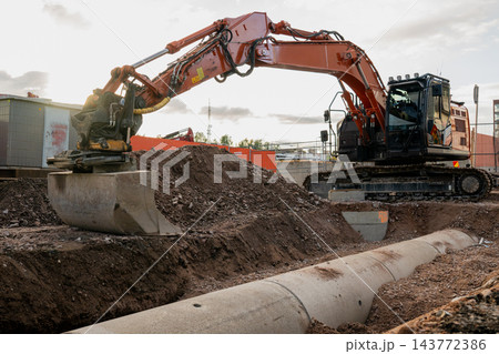 Excavator digging a trench for underground pipeline installation at an urban construction site 143772386