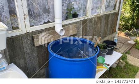 Blue rainwater barrel collecting water from roof gutter at rural house 143772471