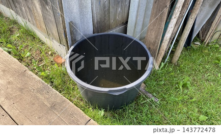 Black plastic water container for rainwater collection in a rural garden Black plastic water container for rainwater collection in a rural garden 143772478