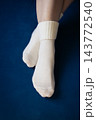 Woman crossing legs in white socks. Girl legs in cozy wool socks on blue background. Cozy autumn lifestyle. Woven socks on woman legs. Woman holding feet on blue sofa. Winter fashion. 143772540