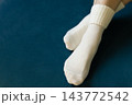 Woman crossing legs in white socks. Girl legs in cozy wool socks on blue background. Cozy autumn lifestyle. Woven socks on woman legs. Woman holding feet on blue sofa. Winter fashion. 143772542
