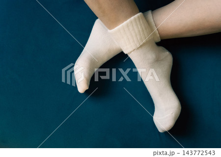 Woman crossing legs in white socks. Girl legs in cozy wool socks on blue background. Cozy autumn lifestyle. Woven socks on woman legs. Woman holding feet on blue sofa. Winter fashion. Woman crossing legs in white socks. Girl legs in cozy wool socks on blue background. Cozy autumn lifestyle. Woven socks on woman legs. Woman holding feet on blue sofa. Winter fashion. 143772543