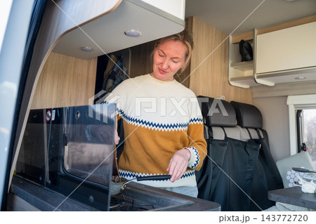 Young woman cooking breakfast inside modern camper van kitchen during road trip adventure Young woman cooking breakfast inside modern camper van kitchen during road trip adventure 143772720