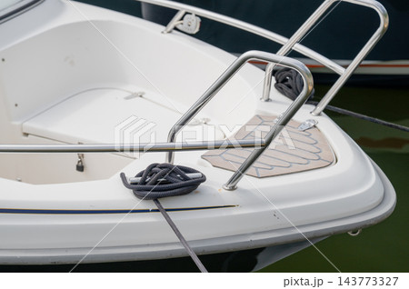 White motorboat stern with stainless steel railing and mooring rope in marina water White motorboat stern with stainless steel railing and mooring rope in marina water 143773327