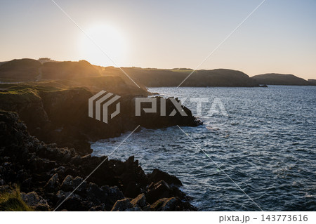 rocky coastline at sunset with ocean waves and golden sunlight over cliffs in scenic coastal landscape 143773616