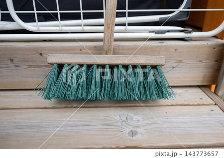 Outdoor broom with wooden handle and green bristles on wooden deck near railing 143773657