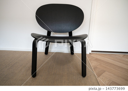 Modern black wooden chair in minimalist interior on carpet near white wall Modern black wooden chair in minimalist interior on carpet near white wall 143773699