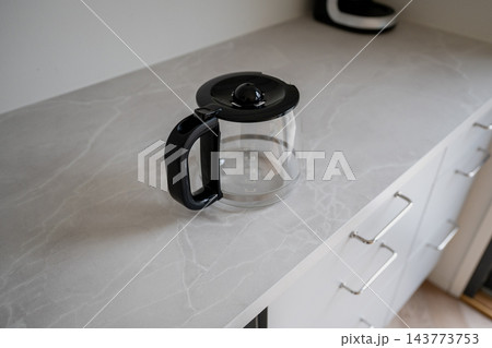 Glass coffee pot with black handle on light kitchen countertop minimalist interior scene 143773753