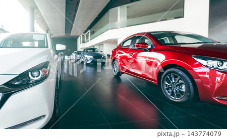 New red and white cars displayed in a modern luxury automobile showroom. Dealership inventory for customers seeking vehicle purchase, leasing, rental and financing. Automotive retail inventory. New red and white cars displayed in a modern luxury automobile showroom. Dealership inventory for customers seeking vehicle purchase, leasing, rental and financing. Automotive retail inventory. 143774079