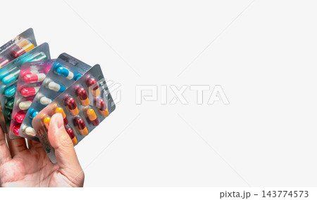Hand holding blister packs of antibiotic capsules in yellow and burgundy, pink and white, blue and white, and green, with silver pharmaceutical packaging for antimicrobial resistance awareness. 143774573