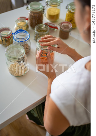 Woman closes a glass jar filled with red lentils using a metal clasp lid in the kitchen. Airtight food storage and reusable containers help organize pantry supplies and reduce packaging waste Woman closes a glass jar filled with red lentils using a metal clasp lid in the kitchen. Airtight food storage and reusable containers help organize pantry supplies and reduce packaging waste 143775173