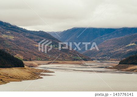 Exposed sandy banks with layered patterns beside Zhinvali Reservoir and cloudy mountains, Georgia Exposed sandy banks with layered patterns beside Zhinvali Reservoir and cloudy mountains, Georgia 143776141