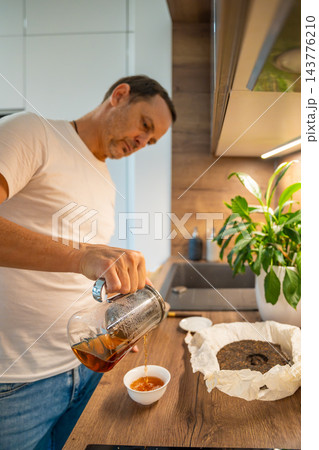 A man pours amber puer tea from a glass teapot into a white cup. Serving tea brewed with aged mandarin peel completes the home brewing ritual. 143776210