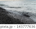 Sea wave with foam on a pebble beach. Wet bright shining different colored pebble stones and sea foam 143777636