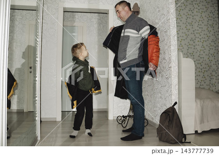 A child in a yellow jacket returns from school with their dad, takes off their outerwear, and goes inside their home. A child in a yellow jacket returns from school with their dad, takes off their outerwear, and goes inside their home. 143777739