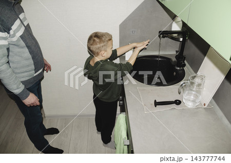 A child returns from school and, together with their dad, washes their hands and face in the sink in the modern kitchen of their home. A child returns from school and, together with their dad, washes their hands and face in the sink in the modern kitchen of their home. 143777744