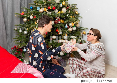 A couple sits near a Christmas tree on Christmas Day. They are exchanging gifts and enjoying the holiday spirit. The room has decorations and a festive atmosphere A couple sits near a Christmas tree on Christmas Day. They are exchanging gifts and enjoying the holiday spirit. The room has decorations and a festive atmosphere 143777961