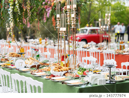 Elegant outdoor wedding banquet with long dining tables, white chairs and abundant floral arrangements. 143777974
