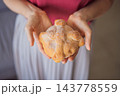 Woman holding a round pan de muerto with a raised dough bone design. 143778559