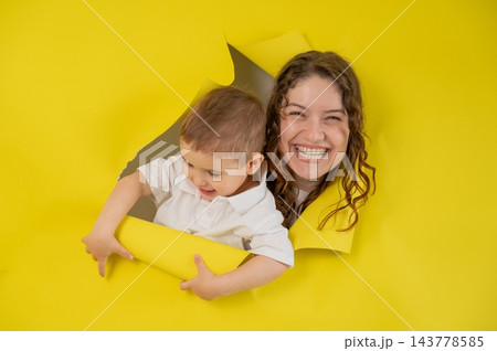 Caucasian little boy and his mother tearing yellow paper background. Caucasian little boy and his mother tearing yellow paper background. 143778585