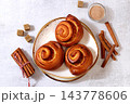 Cinnamon rolls on concrete table, accompanied by cinnamon sticks and burnt sugar, traditional autumn and winter dessert for the cold season. Ideal as a design template or for a shop window display, 143778606