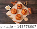 Delicious hot buns rolls on a wooden table, accompanied by cinnamon sticks and burnt sugar, traditional autumn and winter dessert for the cold season. Ideal as a design template 143778607