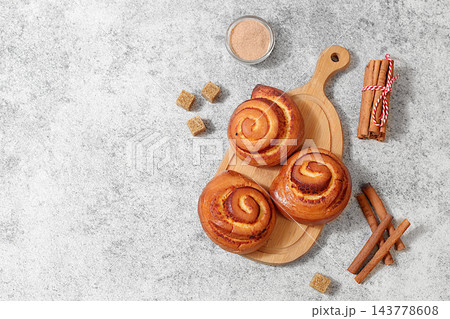 Delicious hot buns rolls on concrete table, accompanied by cinnamon sticks and burnt sugar, traditional autumn and winter dessert for the cold season. Ideal as a design template 143778608